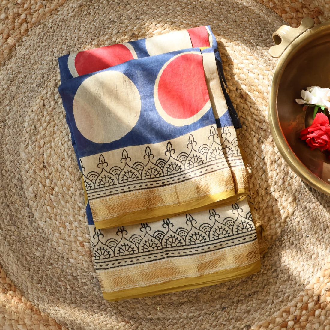 Colorful patterned fabric draped over a wooden cross in a garden setting with a house in the background.