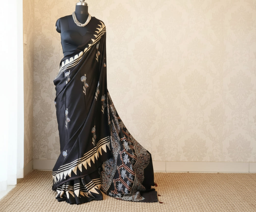 Woman in a black and white patterned saree standing in front of a glass wall with greenery outside.